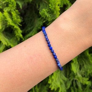 Puede incluir: Un brazalete de piedras preciosas azules hecho con pequeñas cuentas facetadas. El brazalete se lleva en la muñeca.