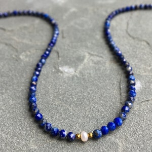 Lapis lazuli beaded necklace with 3mm faceted navy blue beads and a white pearl in the middle. There are 2mm gold hematite beads at each side of the pearl.