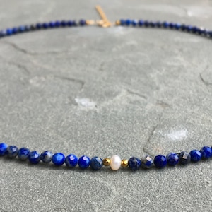 Lapis lazuli beaded necklace with 3mm faceted navy blue beads and a white pearl in the middle. There are 2mm gold hematite beads at each side of the pearl. The necklace has gold clasp and extender chain.