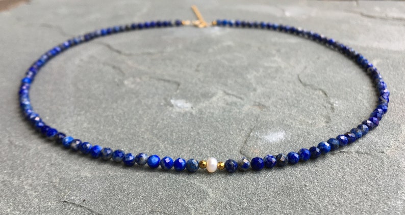 Lapis lazuli beaded necklace with 3mm faceted navy blue beads and a white pearl in the middle. There are 2mm gold hematite beads at each side of the pearl. The necklace has gold clasp and extender chain.