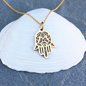 Könnte beinhalten: Eine goldene Kettenkette mit einem zarten, verzierten Hamsa-Hand-Anhänger. Der Anhänger ist ein Ausschnitt mit filigranen Details.