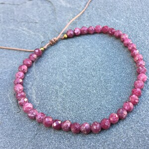 Dainty ruby beaded bracelet with deep red faceted gemstones and small gold spacer beads on an adjustable cord, handmade gemstone jewelry for women, elegant stacking bracelet or solitaire statement piece.