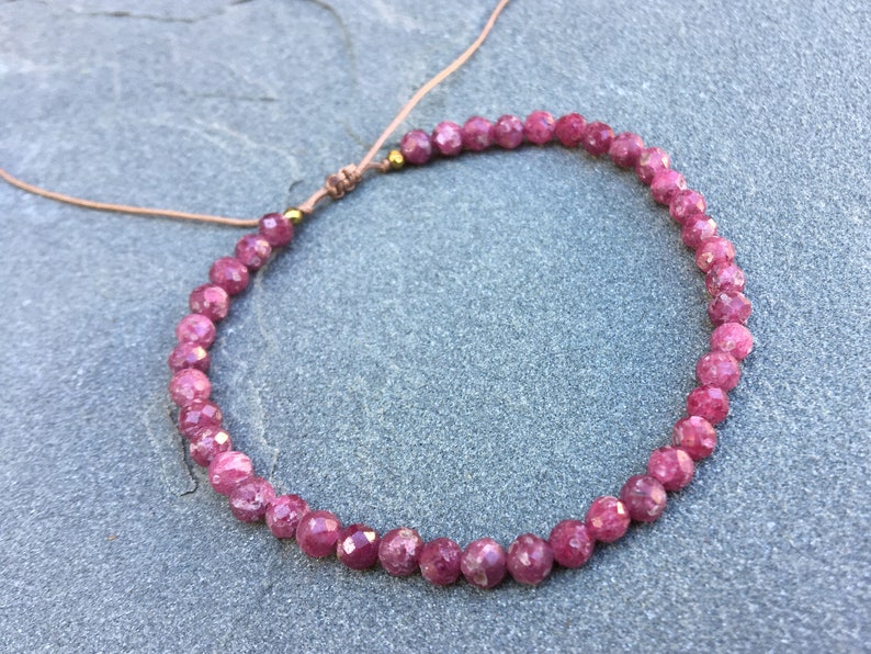 Dainty ruby beaded bracelet with deep red faceted gemstones and small gold spacer beads on an adjustable cord, handmade gemstone jewelry for women, elegant stacking bracelet or solitaire statement piece.