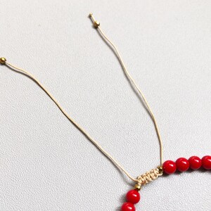 A red beaded bracelet with a sliding knot closure. The bracelet is made of small, round 4mm coral beads and is strung on a thin, beige cord.