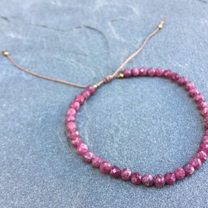 Dainty ruby beaded bracelet with deep red faceted gemstones and small gold spacer beads on an adjustable cord, handmade gemstone jewelry for women, elegant stacking bracelet or solitaire statement piece.