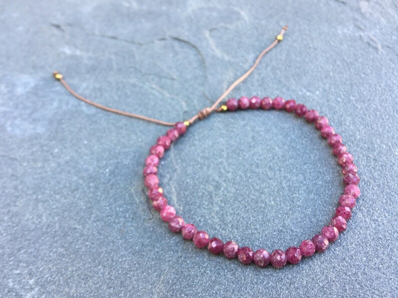 Dainty ruby beaded bracelet with deep red faceted gemstones and small gold spacer beads on an adjustable cord, handmade gemstone jewelry for women, elegant stacking bracelet or solitaire statement piece.