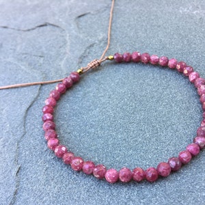 Dainty ruby beaded bracelet with deep red faceted gemstones and small gold spacer beads on an adjustable cord, handmade gemstone jewelry for women, elegant stacking bracelet or solitaire statement piece.