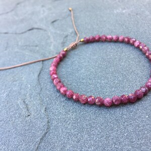 Dainty ruby beaded bracelet with deep red faceted gemstones and small gold spacer beads on an adjustable cord, handmade gemstone jewelry for women, elegant stacking bracelet or solitaire statement piece.