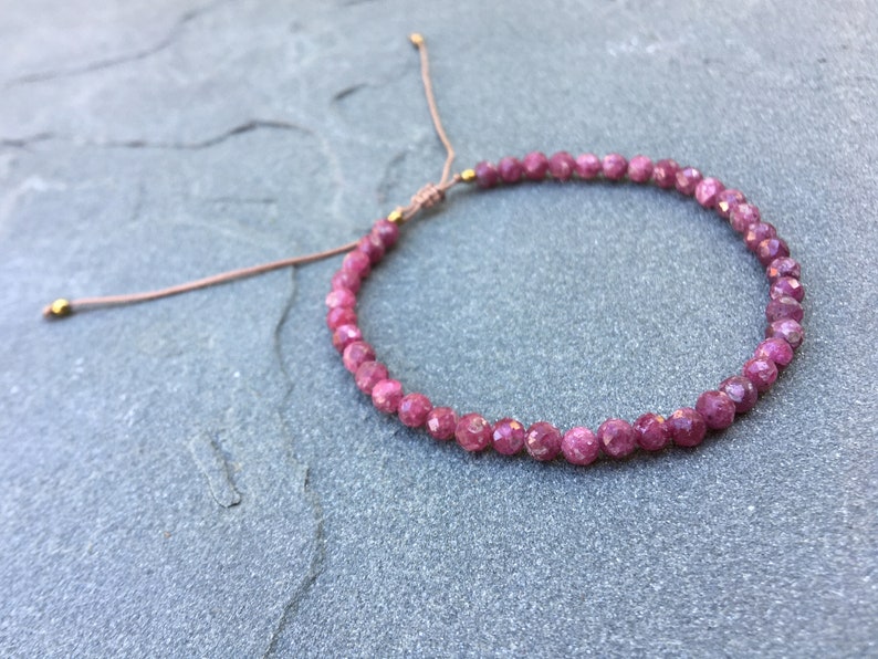 Dainty ruby beaded bracelet with deep red faceted gemstones and small gold spacer beads on an adjustable cord, handmade gemstone jewelry for women, elegant stacking bracelet or solitaire statement piece.