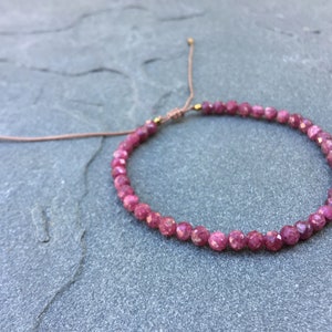 Dainty ruby beaded bracelet with deep red faceted gemstones and small gold spacer beads on an adjustable cord — handmade gemstone jewelry for women, elegant stacking bracelet or solitaire statement piece.