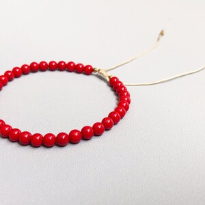A red beaded bracelet with a sliding knot closure. The bracelet is made of small, round, red coral beads and has a thin, beige cord.