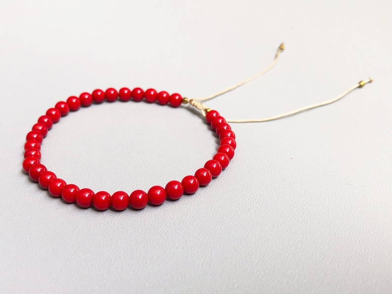 A red beaded bracelet with a sliding knot closure. The bracelet is made of small, round, red coral beads and has a thin, beige cord.