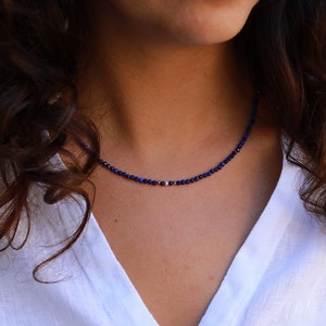 Lapis lazuli beaded necklace with 3mm faceted navy blue beads and a white pearl in the middle. There are 2mm gold hematite beads at each side of the pearl. The necklace has gold clasp and extender chain.