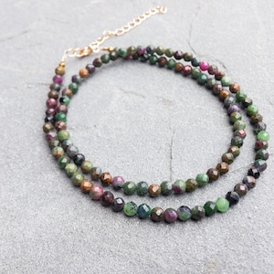 May include: A double-strand necklace made of faceted green, brown, and pink gemstone beads. The necklace is made with a gold-tone clasp.