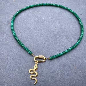 May include: A green gemstone beaded necklace with a gold snake charm. The necklace is made of small, faceted beads and has a simple, elegant design.