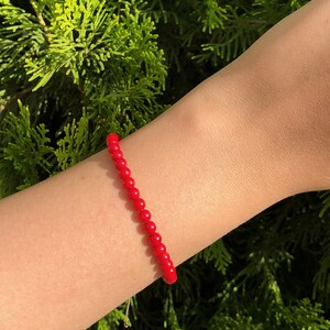 Dainty red coral beaded bracelet with adjustable cord, featuring vibrant natural coral gemstones, styled on wrist against a neutral background