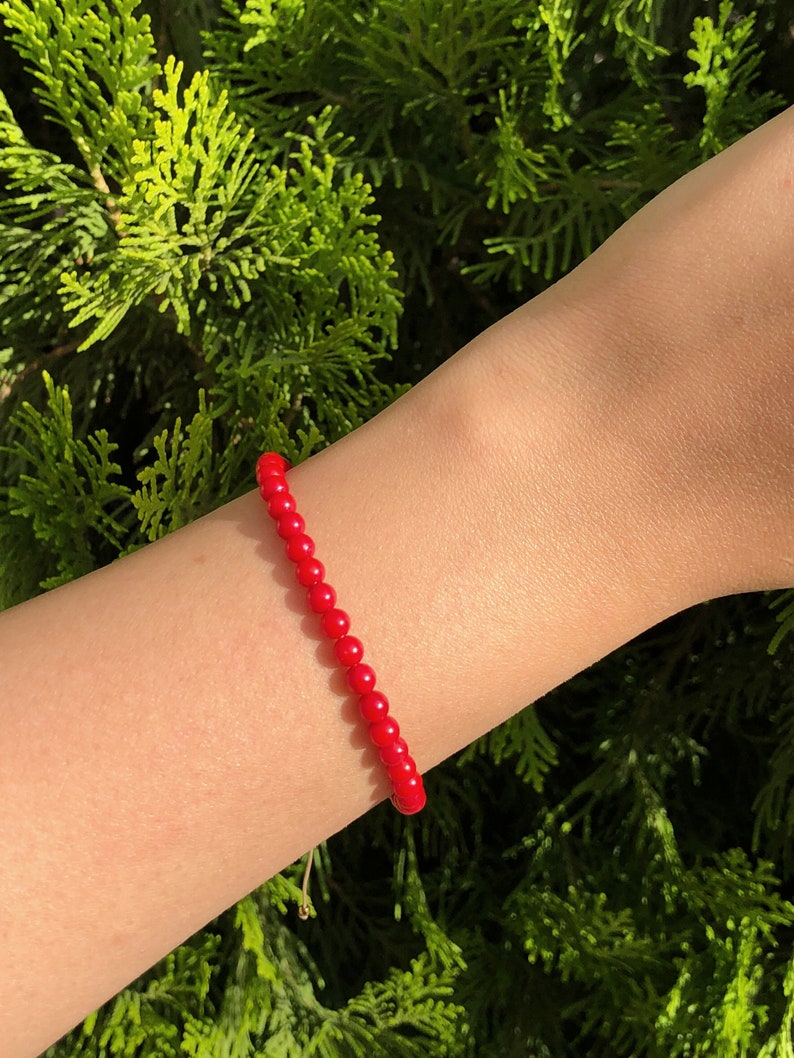 Dainty red coral beaded bracelet with adjustable cord, featuring vibrant natural coral gemstones, styled on wrist against a neutral background