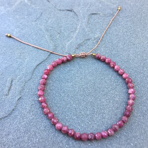 Dainty ruby beaded bracelet with deep red faceted gemstones and small gold spacer beads on an adjustable cord, handmade gemstone jewelry for women, elegant stacking bracelet or solitaire statement piece.