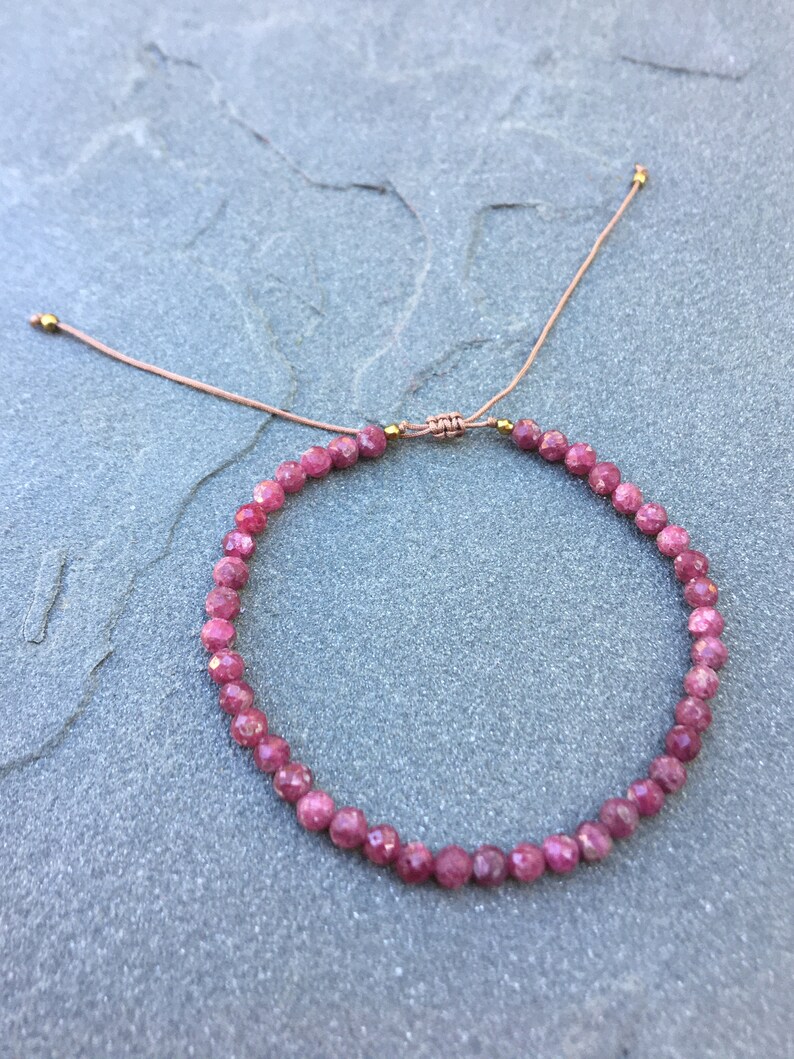 Dainty ruby beaded bracelet with deep red faceted gemstones and small gold spacer beads on an adjustable cord, handmade gemstone jewelry for women, elegant stacking bracelet or solitaire statement piece.