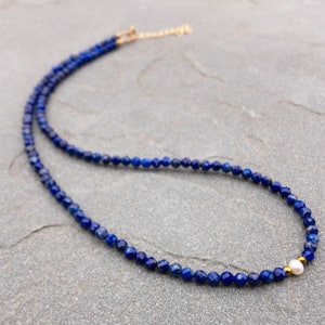 Lapis lazuli beaded necklace with 3mm faceted navy blue beads and a white pearl in the middle. There are 2mm gold hematite beads at each side of the pearl. The necklace has gold clasp and extender chain.