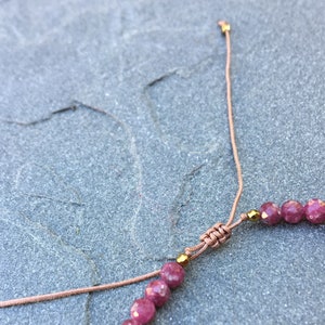 Dainty ruby beaded bracelet with deep red faceted gemstones and small gold spacer beads on an adjustable cord, handmade gemstone jewelry for women, elegant stacking bracelet or solitaire statement piece.