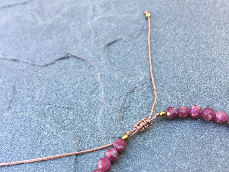 Dainty ruby beaded bracelet with deep red faceted gemstones and small gold spacer beads on an adjustable cord, handmade gemstone jewelry for women, elegant stacking bracelet or solitaire statement piece.