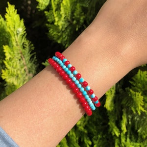 May include: Three stacked bracelets with red and blue beads. The bracelets are made of small, round beads.