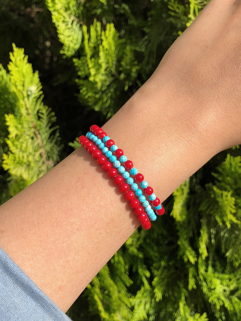 May include: Three stacked bracelets with red and blue beads. The bracelets are made of small, round beads.
