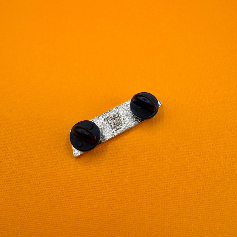 Op de afbeelding: Een rechthoekige metalen pin met een getextureerde zilveren afwerking en twee zwarte rubberen sluitingen. In het midden van de pin staat de tekst Funko in reli&euml;f, met het woord Funko eronder herhaald in een kleiner, gestileerd lettertype.