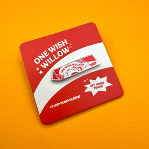 Op de afbeelding: Een rechthoekige emaille speld met de tekst ONE WISH WILLOW en bloemillustraties in rood en wit. De speld is bevestigd op een rood-witte presentatiekaart met de tekst ONE WISH WILLOW, GET YOURS TODAY en FUNKYPUNKYDESIGNS.
