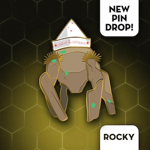 Puede incluir: Un pin de esmalte marrón y dorado que representa un personaje con un sombrero blanco que dice "Savior of the Universe". El pin tiene un contorno dorado y detalles verdes. También se ven las palabras "NEW PIN DROP!" y "ROCKY".
