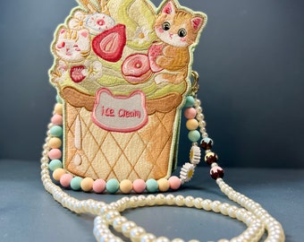 Puede incluir: Un bolso bordado con forma de cono de helado con un diseño de gato. El bolso presenta una bola de helado verde claro, una fresa y dos gatos. El bolso tiene una correa de cuentas con cuentas de colores pastel y una correa de collar de perlas.