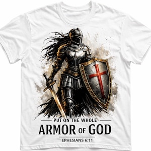 Può includere: T-shirt bianca con un guerriero in armatura completa, con una spada e uno scudo con una croce rossa. Il testo recita "PUT ON THE WHOLE ARMOR OF GOD" e "EPHESIANS 6:11". Il design presenta toni metallici e scuri.