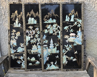 May include: Four-panel black lacquer screen with gold trim. Each panel features a landscape scene with mountains, pagodas, trees, and figures, accented with mother-of-pearl and gold details. The artwork is displayed on a wooden bench.
