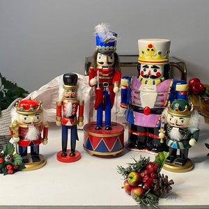 May include: A group of five decorative nutcrackers in different sizes and styles. The nutcrackers are painted in bright colours, including red, blue, green, and gold, with detailed features. Some are dressed as soldiers, others wear crowns, ideal for festive decorations.