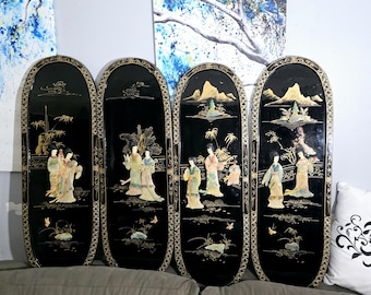 May include: Four-panel black lacquer screen with oval panels. Each panel features a detailed scene with figures in traditional dress, mountains, and trees, accented with gold and mother-of-pearl. The screen is a decorative room divider.