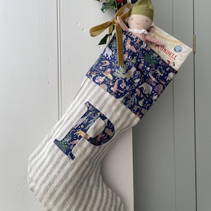 Op de afbeelding: Een kerstsok met een gestreepte body en een marineblauwe top met een grillige dierenprint. De letter "P" is op de voorkant aangebracht. De sok is gevuld met een boek en een pop en versierd met hulst.