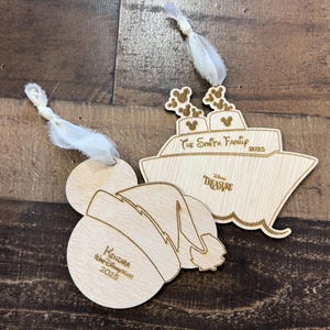 Pode incluir: Dois enfeites de madeira da Disney com fitas brancas para pendurar. Um é um navio de cruzeiro com "The Smith Family 2025" e "Disney Treasure" gravados. O outro é um design de orelha do Mickey Mouse com "Kendra Walt Disney World 2025."