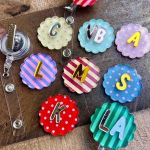 Puede incluir: Una colecci&oacute;n de coloridos portatarjetas con bordes festoneados, cada uno con una letra diferente. Los portatarjetas tienen varios patrones, incluyendo rayas y lunares, y son en tonos de rosa, azul, amarillo y verde. Las letras son en plata y amarillo.