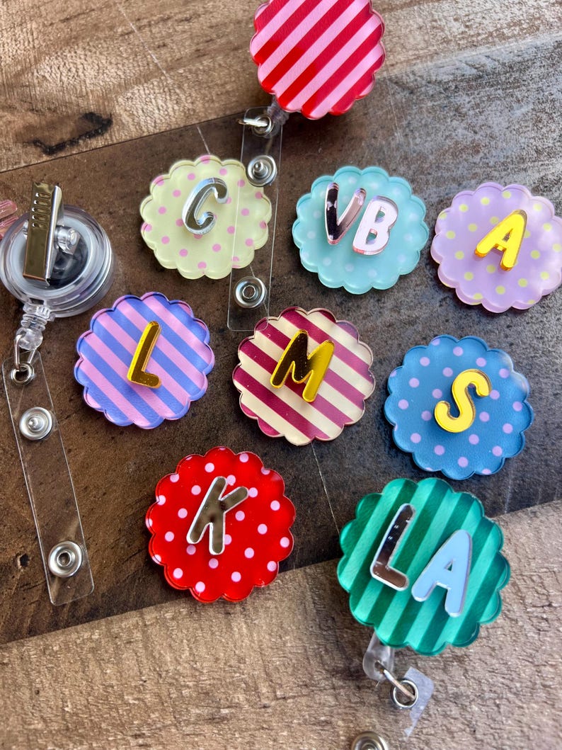 Puede incluir: Una colecci&oacute;n de coloridos portatarjetas con bordes festoneados, cada uno con una letra diferente. Los portatarjetas tienen varios patrones, incluyendo rayas y lunares, y son en tonos de rosa, azul, amarillo y verde. Las letras son en plata y amarillo.