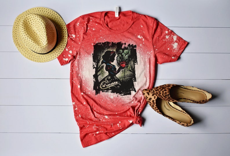 Op de afbeelding: Rood T-shirt met een bleekmiddel-spatpatroon met een afbeelding van Sneeuwwitje en de boze koningin. Het shirt is onderaan geknoopt. Een strohoed en luipaardprint schoenen zijn ook afgebeeld.