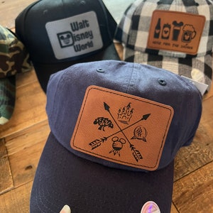 May include: Three baseball caps with different designs. The first cap is black with a white patch that says "Walt Disney World" and a Mickey Mouse silhouette. The second cap is white and black checkered with a brown patch that says "Here for the good times" and has a beer mug, a bottle, and a Mickey Mouse silhouette. The third cap is navy blue with a brown patch that has a Mickey Mouse silhouette, a castle, a tree, and a ball with a cross through it. The patch also has arrows pointing in different directions.