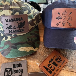May include: Four different brown leather patches with Disney-themed designs. The patches feature the text "Hakuna Matata", "Walt Disney World", "Here for the Drinks", and a castle with arrows and Mickey Mouse.