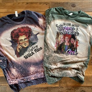 Op de afbeelding: Twee shirts met lange mouwen met bleekmiddelspatten. Het eerste shirt is donkerblauw met een afbeelding van de Wicked Witch of the West uit de film The Wizard of Oz met de tekst "Resting Witch Face". Het tweede shirt is groen met een afbeelding van de drie heksen uit de film met de tekst "Oh look another Glorious Morning Makes Me Sick".