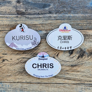 May include: Three Disney name tags with different designs. One features "KURISU" and "TOKYO Disney RESORT" with a Mickey Mouse graphic. Another says "CHRIS" in English and Chinese, with "SHANGHAI Disney RESORT". The last one says "CHRIS" and "ORLANDO, FL" with "Bringing Back The Magic".