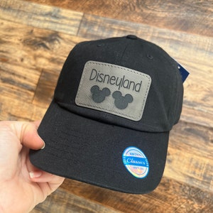 May include: Black baseball cap with a gray leather patch that says "Disneyland" with Mickey Mouse ears. The cap has a blue and white label that says "Kith & Kin Classics Since 1994."