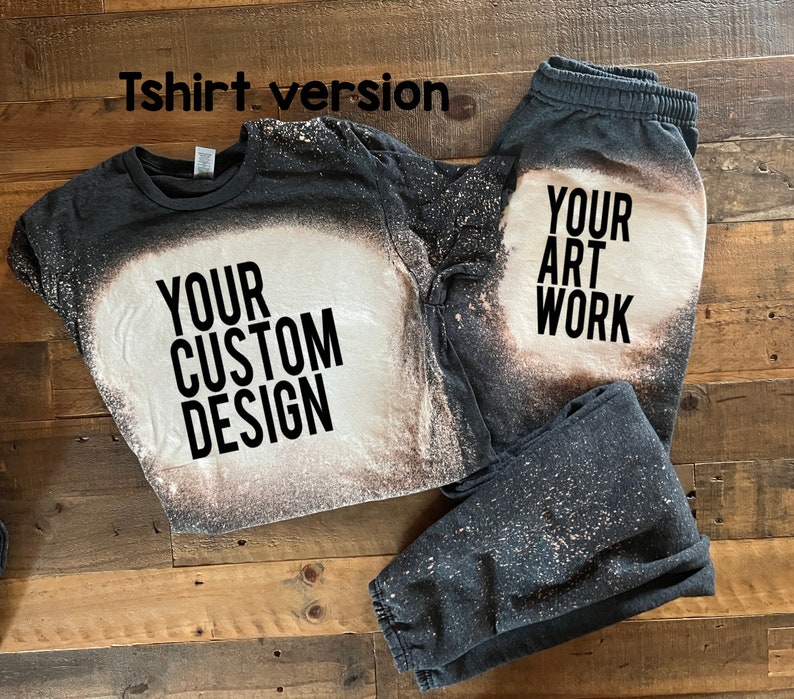 May include: A black t-shirt and sweatpants with a bleach-splattered design. The t-shirt has the text "YOUR CUSTOM DESIGN" printed on it. The sweatpants have the text "YOUR ART WORK" printed on them.