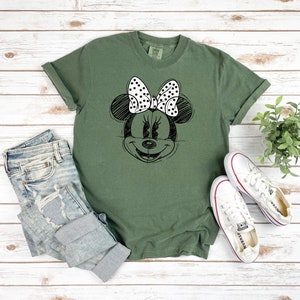 Puede incluir: Una camiseta verde con un dibujo en blanco y negro de Minnie Mouse con un lazo de lunares.