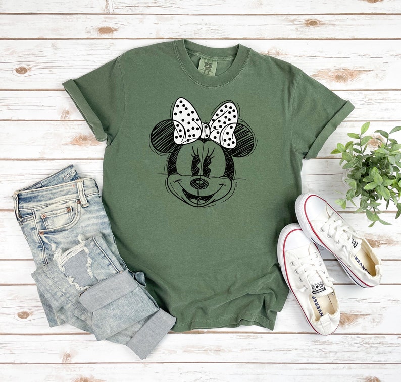Puede incluir: Una camiseta verde con un dibujo en blanco y negro de Minnie Mouse con un lazo de lunares.