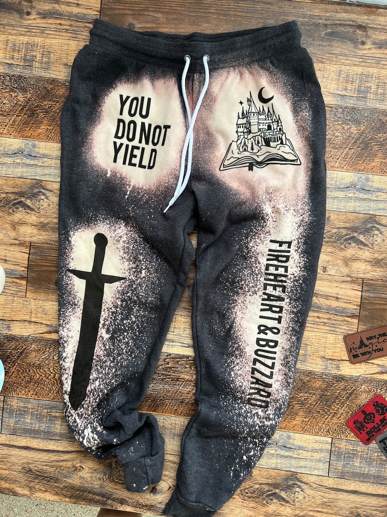 May include: Black sweatpants with a white bleach design. The design includes a castle, a book, a sword, and the text "You Do Not Yield" and "Fireheart & Buzzard".